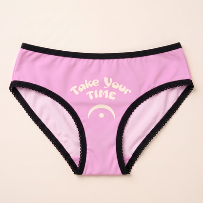 Pink women’s briefs with black trim featuring cream “Take Your Time” text and fermata music symbol
